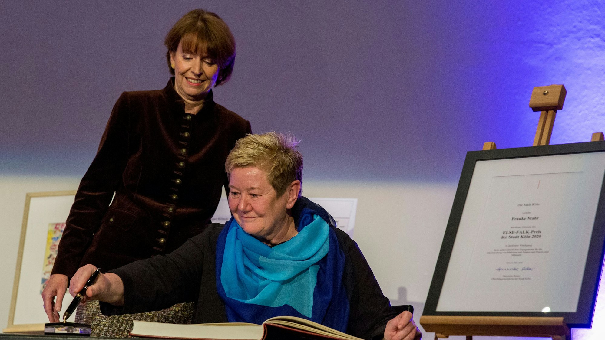 OB Henriette Reker steht bei der Verleihung des Else-Falk-Preises im März 2020 hinter Frauke Mahr, die sich ins Goldene Buch der Stadt Köln einträgt.