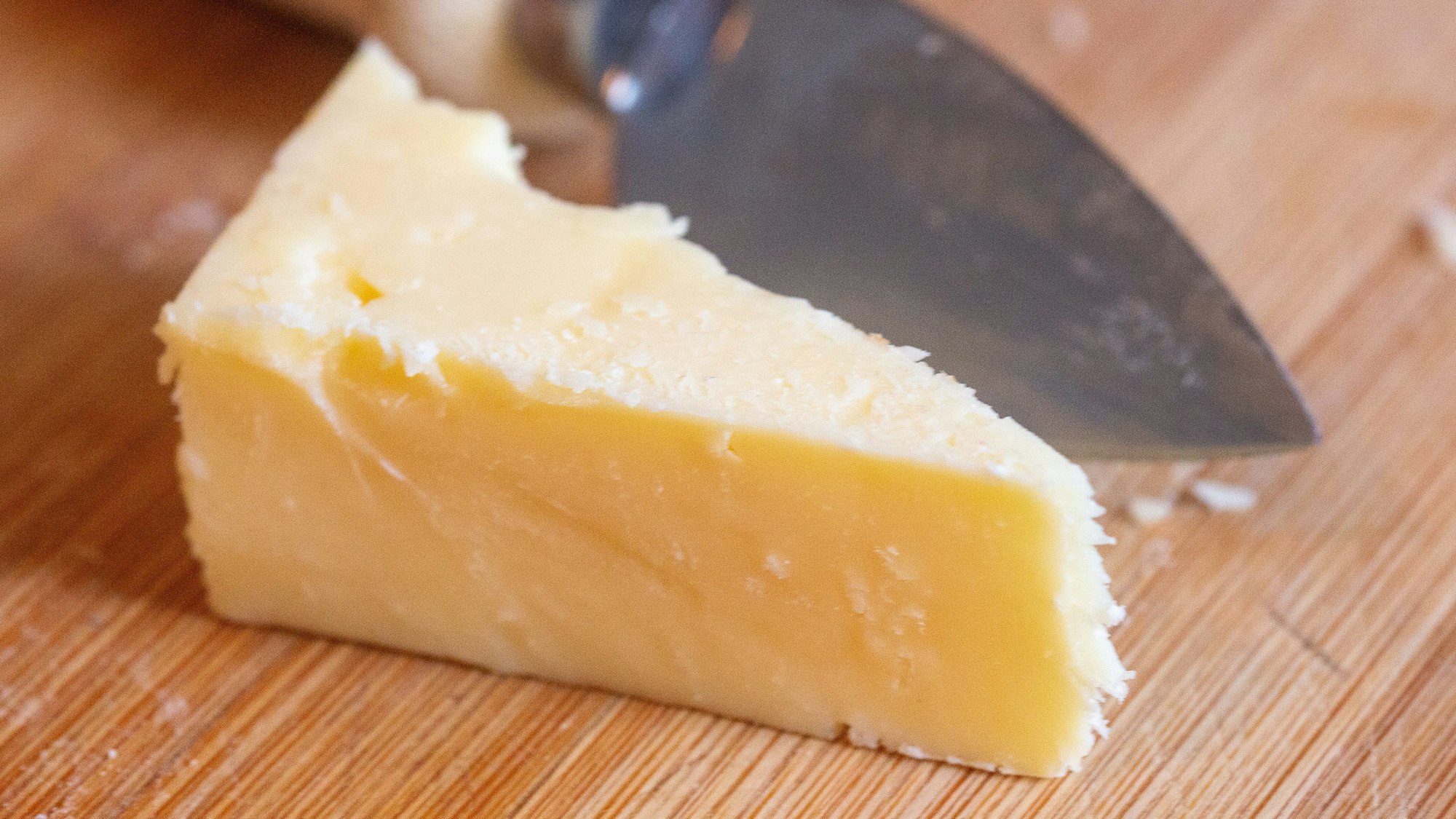 SYMBOLBILD - 02.07.2024, Berlin: ILLUSTRATION - Ein Stück Cheddar-Käse liegt auf einem Brett.