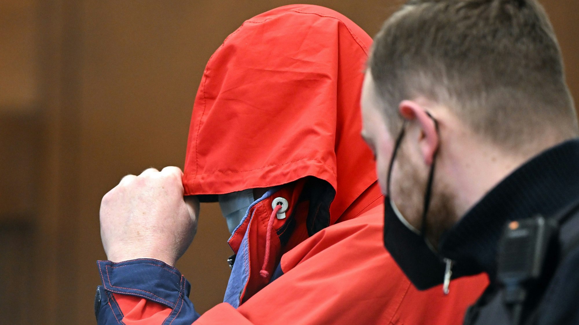 Hans Ue., vom Landgericht Köln 2022 als Serientäter verurteilter Priester des Erzbistums Köln, zieht sich die Kapuze seiner roten Jacke über das Gesicht.