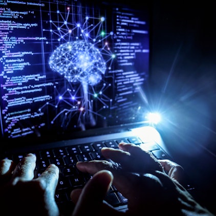 Nordrhein-Westfalen, Köln: Eine Person arbeitet am Rechner, auf dessen Bildschirm ein durch Künstliche Intelligenz generiertes Illustrationsbild mit Code verschiedener Programmiersprachen und einem neuronalen Netzwerk-Diagramm zu sehen ist. (Symbolbild)