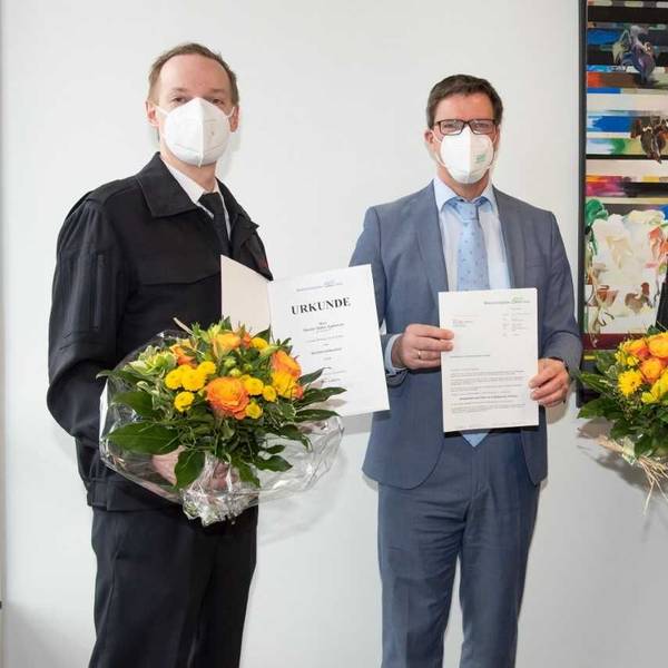 Zwei Männer stehen mit Mund-Nase-Schutz und Urkunden im Kreishaus.