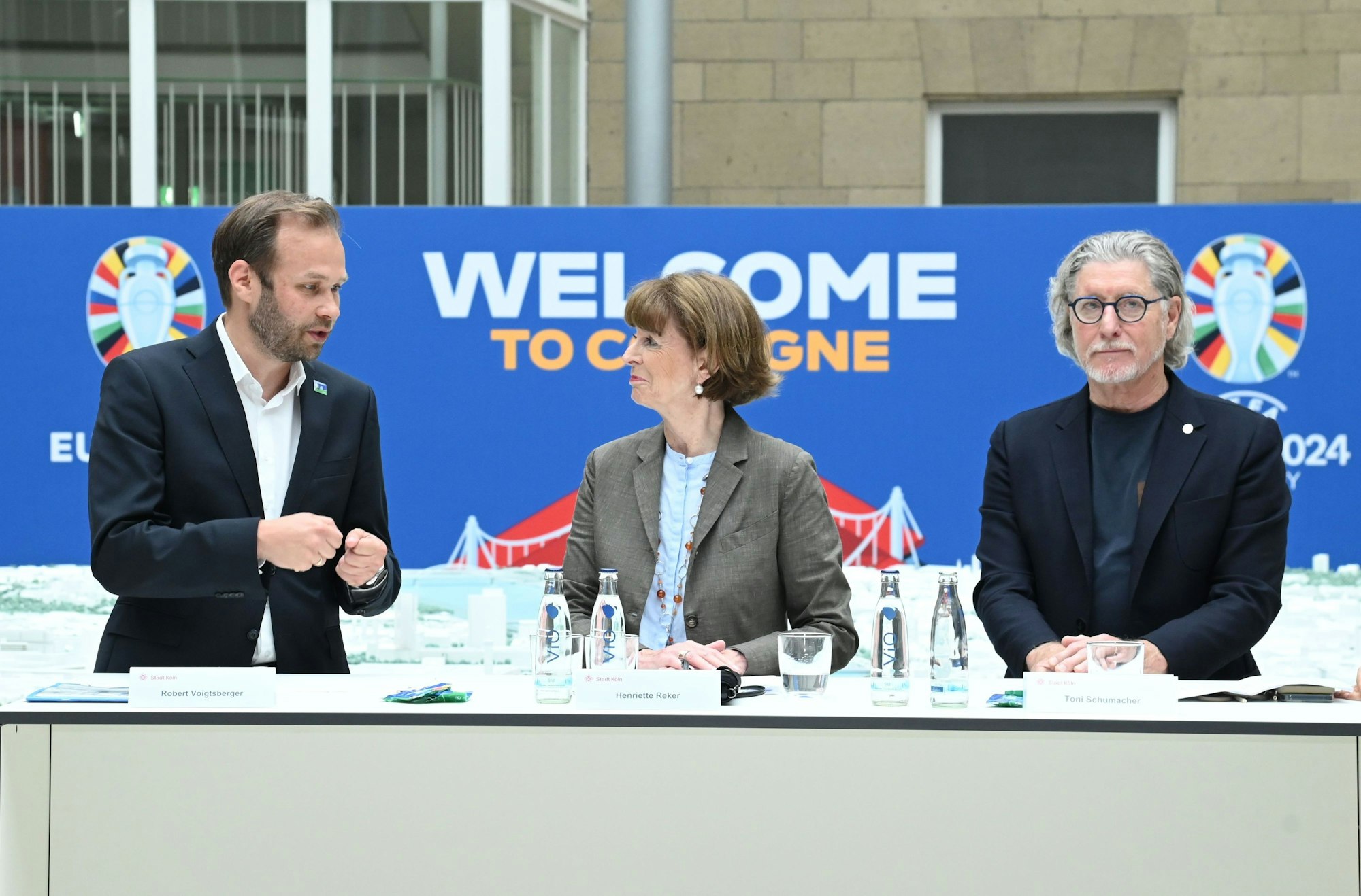 Zu sehen sind von links nach rechts Robert Voigtsberger, OB Reker und Toni Schumacher, die an einem Tisch stehen.