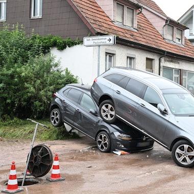 Auf einer Straße in Miedelsbach in Baden-Württemberg stehen Fahrzeuge, die durch ein Hochwasser nach einem Unwetter weggespült wurden.