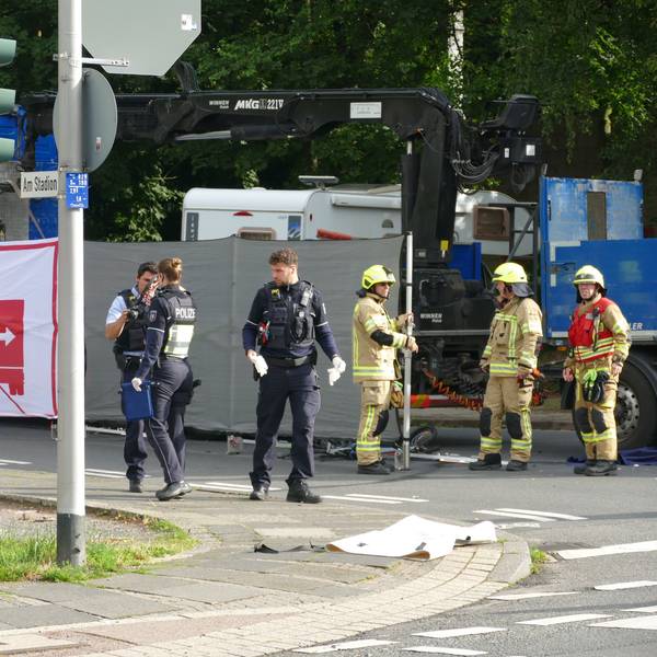 Polizisten und Feuerwehrleute stehen vor einem Lastwagen, vor dem ein Sichtschutz aufgebaut ist.