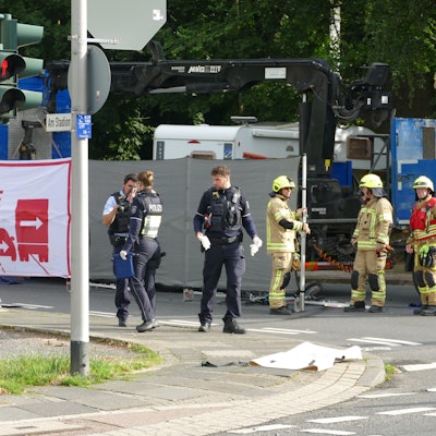 Polizisten und Feuerwehrleute stehen vor einem Lastwagen, vor dem ein Sichtschutz aufgebaut ist.