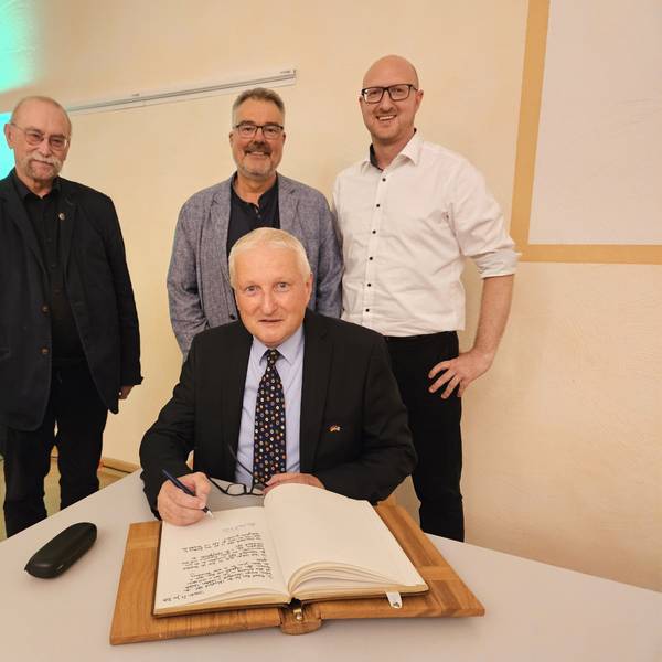 Dr. Michael Röös trägt sich ins Goldene Buch der Stadt Schleiden ein, dahinter stehen Philipp Cuck, Erik Schumacher und Ingo Pfennings.