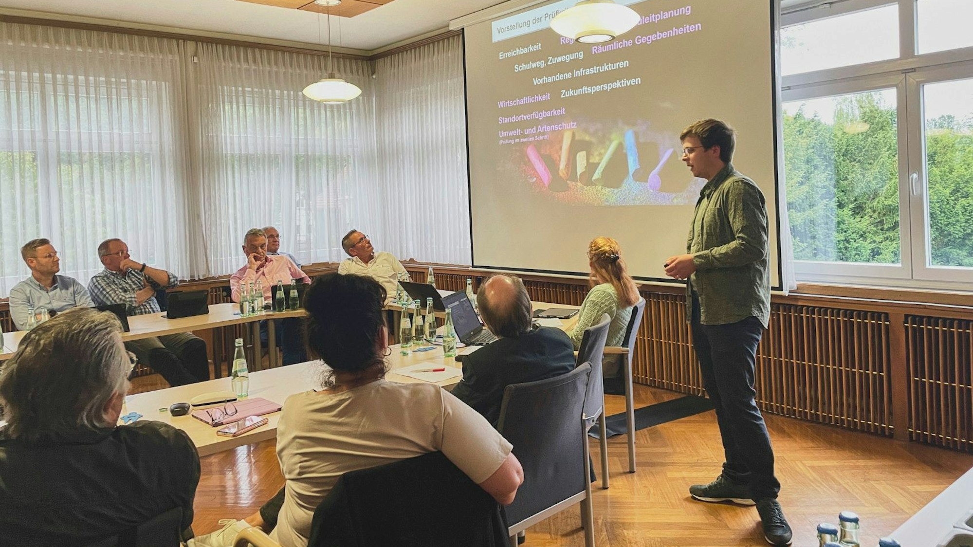 Christian Schmitz vom Planungsbüro PE Becker steht vor einer Leinwand. Hellenthaler Politiker sitzen an Tischen und hören seinem Vortrag zu.