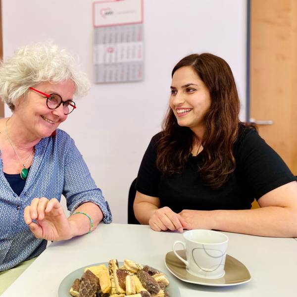Monika Lauer und Khatera Naimi unterhalten sich. Vor ihnen stehen Kekse und eine Kaffeetasse.