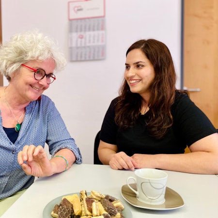 Monika Lauer und Khatera Naimi unterhalten sich. Vor ihnen stehen Kekse und eine Kaffeetasse.