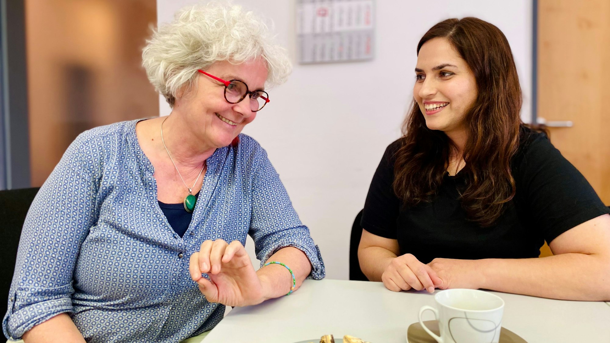 Monika Lauer und Khatera Naimi unterhalten sich. Vor ihnen stehen Kekse und eine Kaffeetasse.