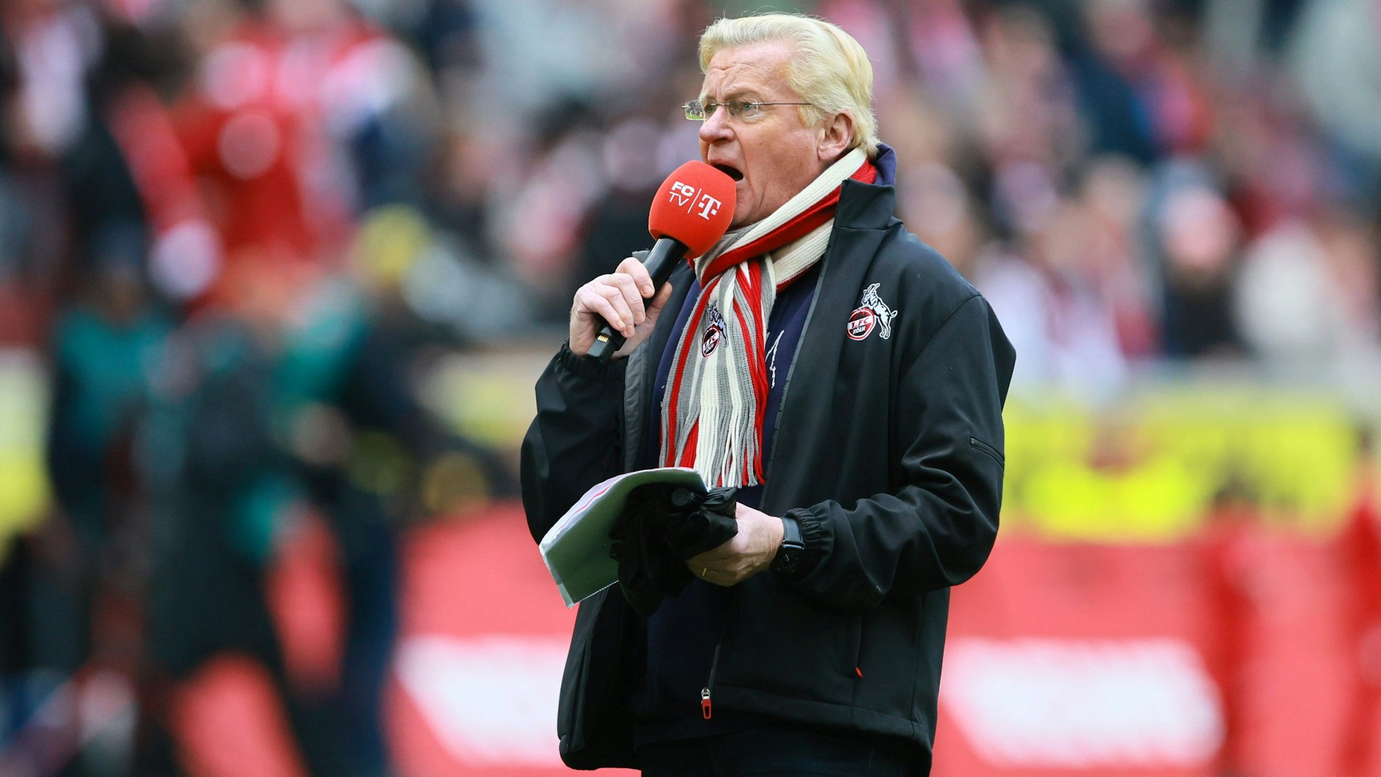 Ein Mann steht in einem Stadion und spricht in ein Mikrofon.