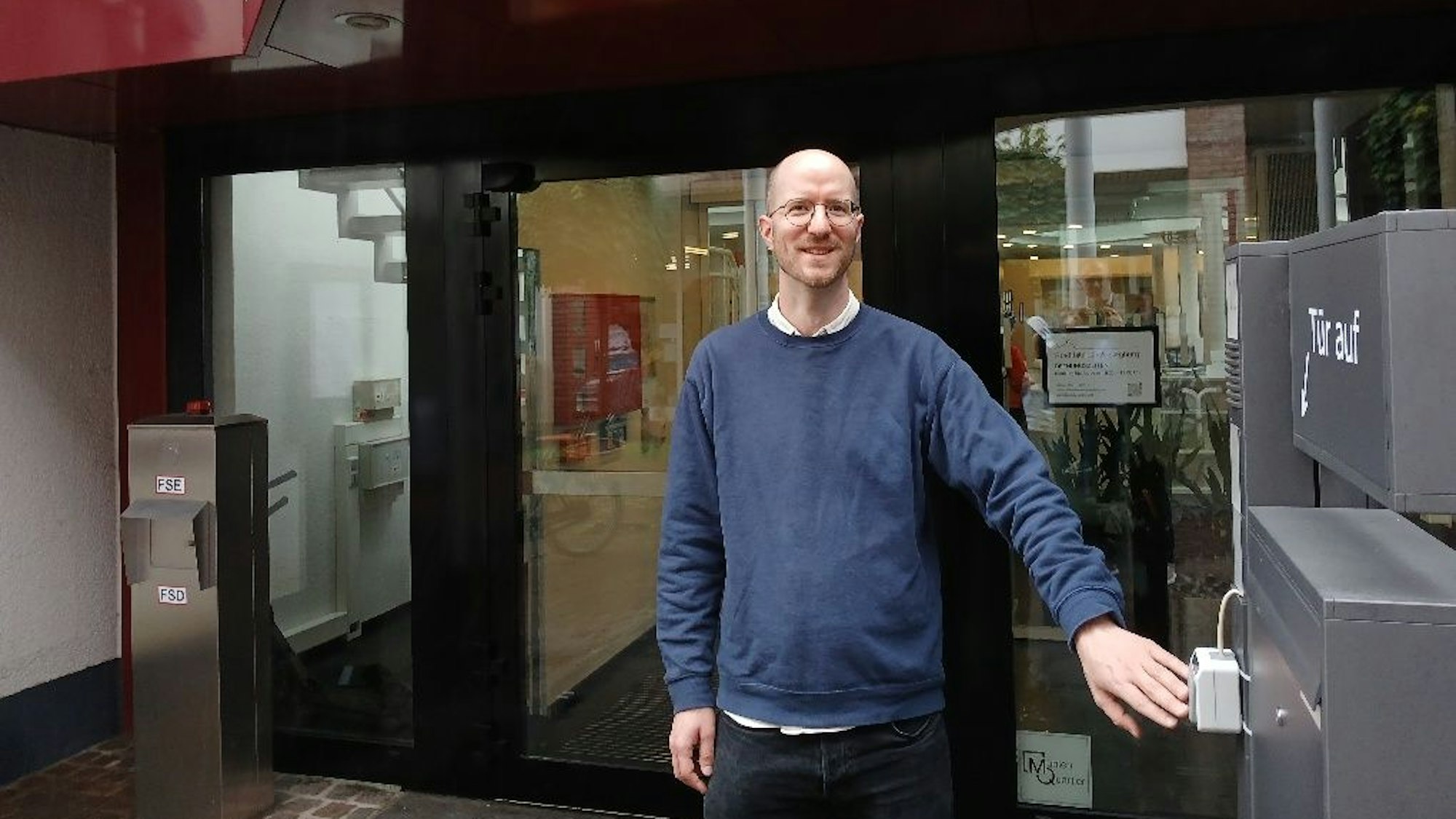 Ein Mann in einem blauen Pullover vor einer Bibliothek