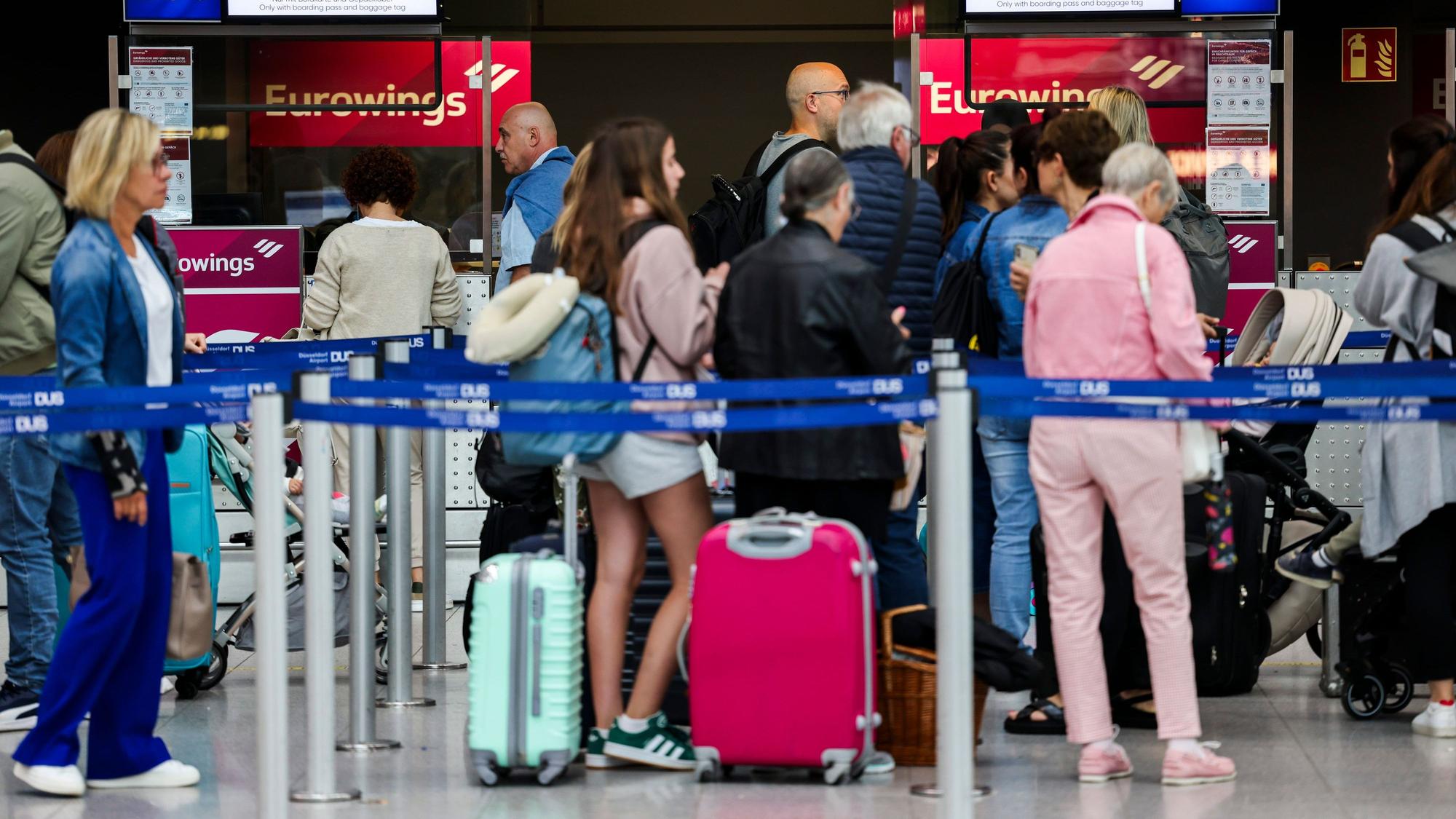 03.07.2024, Nordrhein-Westfalen, Düsseldorf: Passagiere stehen am Flughafen in einer Warteschlange vor den Gepäckaufgabe- und Check-In-Schaltern von Eurowings. Foto: Christoph Reichwein/dpa +++ dpa-Bildfunk +++