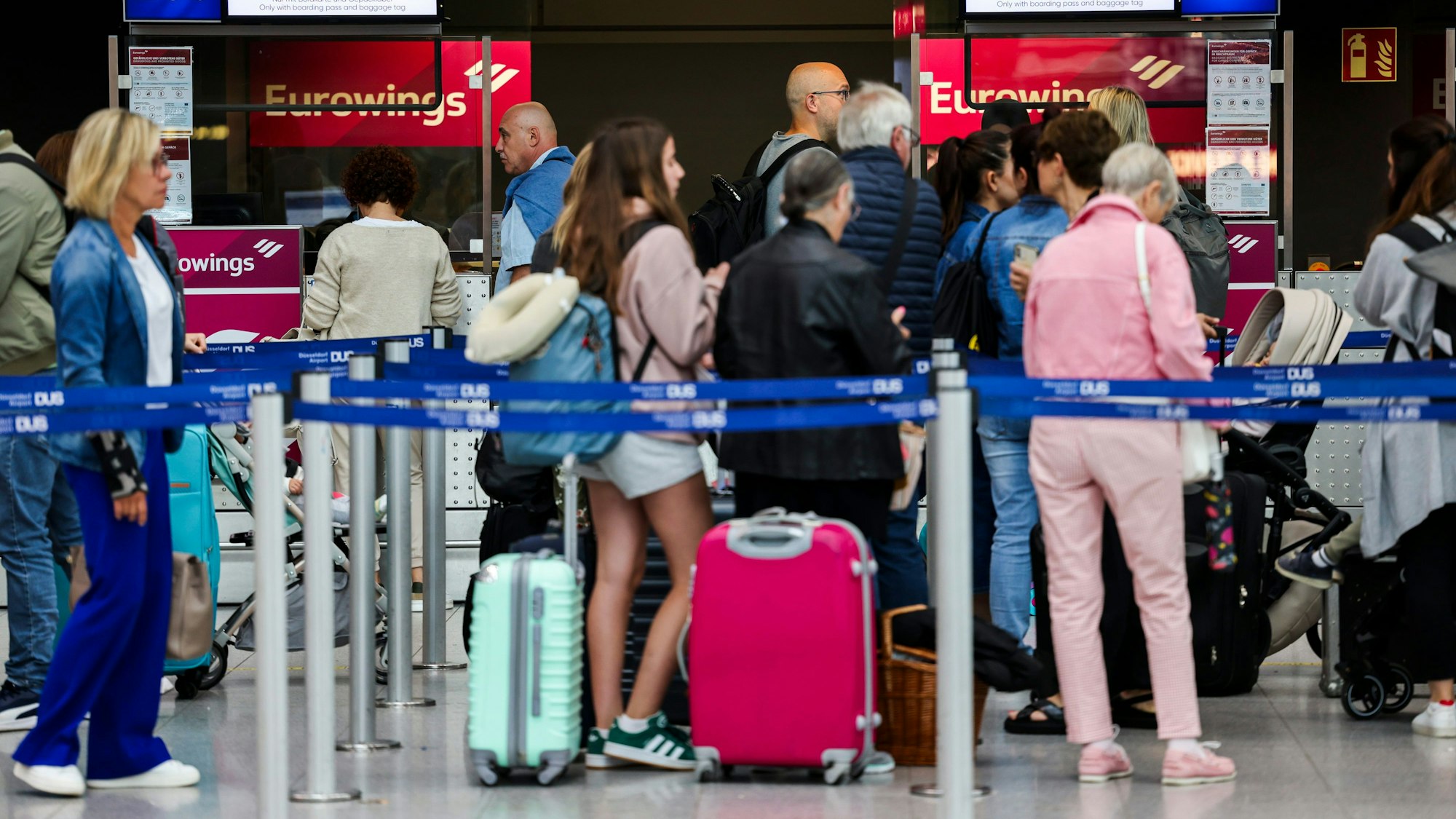 03.07.2024, Nordrhein-Westfalen, Düsseldorf: Passagiere stehen am Flughafen in einer Warteschlange vor den Gepäckaufgabe- und Check-In-Schaltern von Eurowings. Foto: Christoph Reichwein/dpa +++ dpa-Bildfunk +++