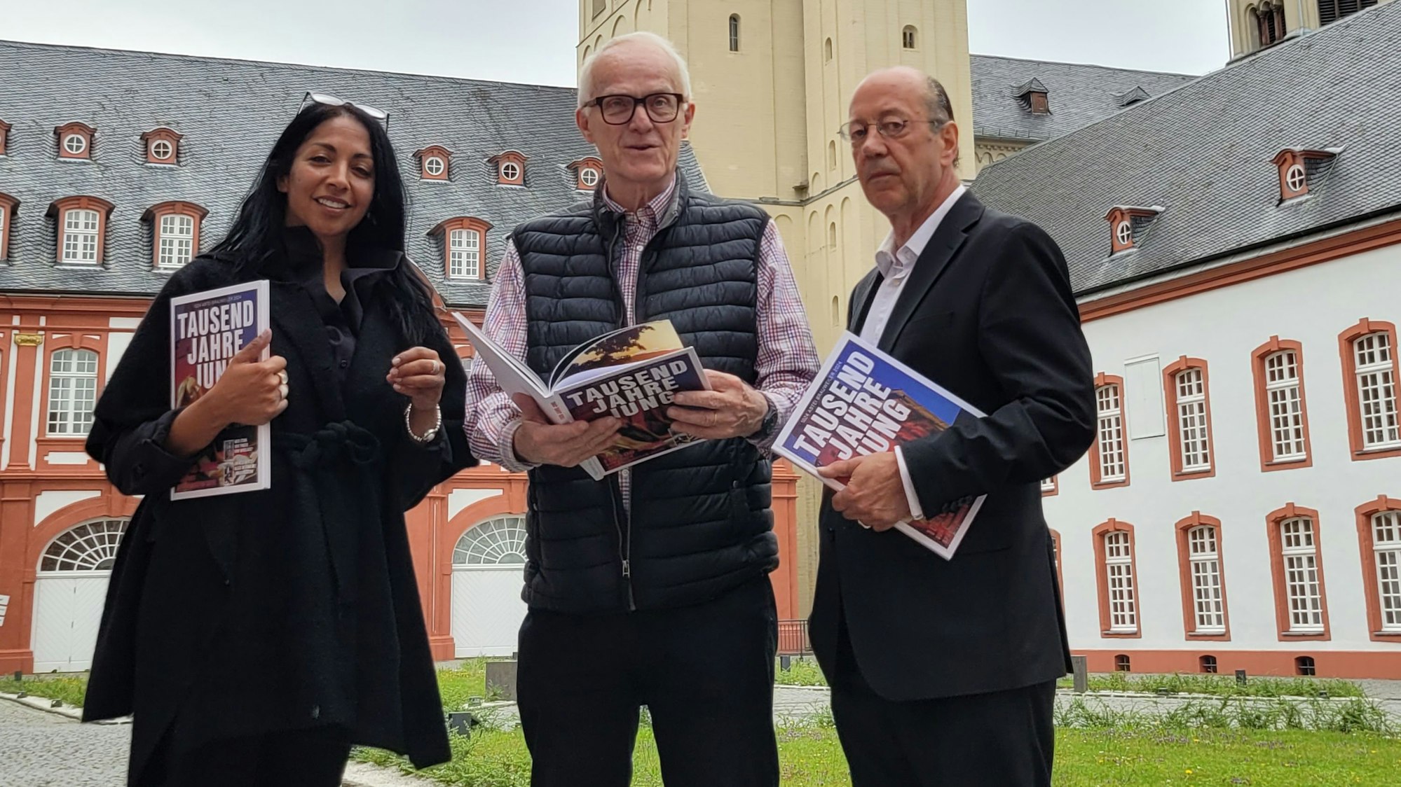 Eine Frau und zwei Männer vor der barocken Fassade der Abtei Brauweiler.