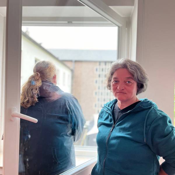 Eine Frau, Monika Wilke, gut in die Kamera, von einer zweiten ist eine Rückenansicht zu sehen, sie schaut aus dem Fenster.