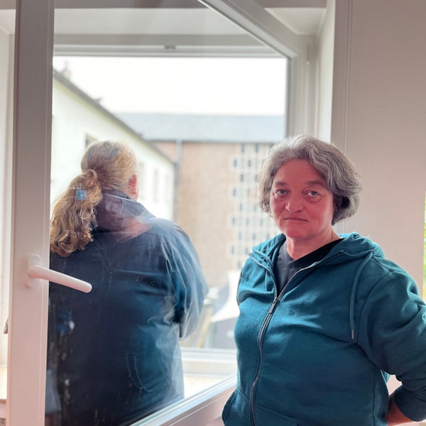 Eine Frau, Monika Wilke, gut in die Kamera, von einer zweiten ist eine Rückenansicht zu sehen, sie schaut aus dem Fenster.