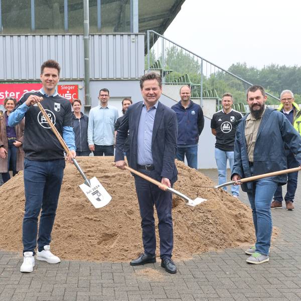 Vier Herren mit Spaten vor einem Sandhaufen.