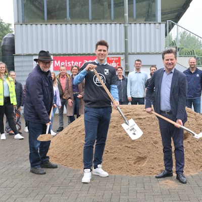 Vier Herren mit Spaten vor einem Sandhaufen.