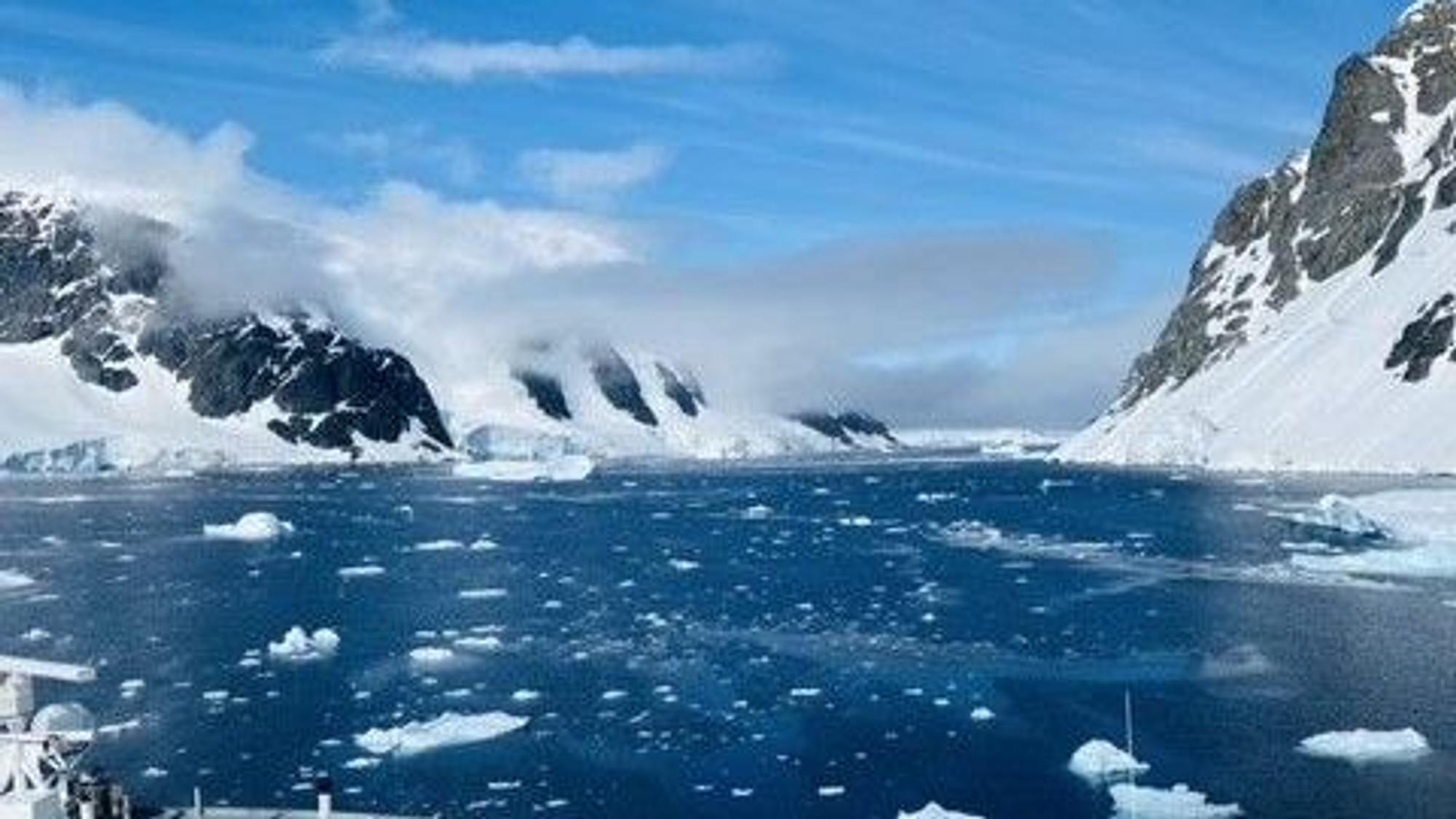 Eine Meerenge, links und rechts teils eisbedeckte Felsen, kleine Eisschollen auf dem Wasser.