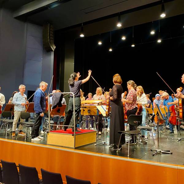 Bar Avni steht auf einem Podest vor dem Orchester. Auch die Musikerinnen und Musiker haben sich erhoben.