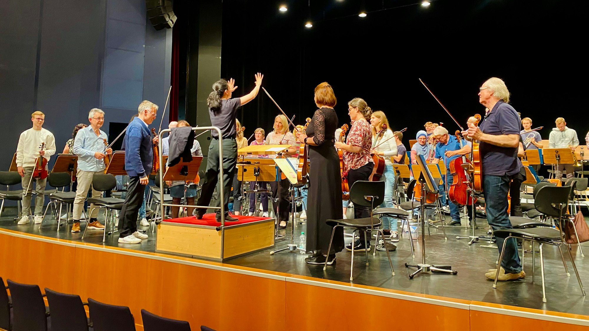 Bar Avni steht auf einem Podest vor dem Orchester. Auch die Musikerinnen und Musiker haben sich erhoben.