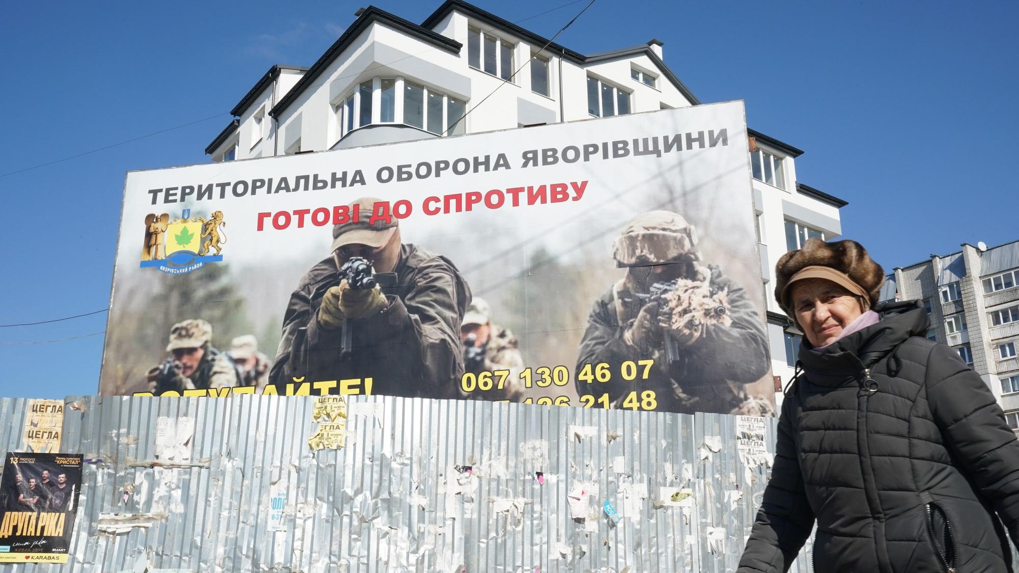 Eine Frau geht an einem Plakat vorbei, auf dem Soldaten im Einsatz zu sehen sind.