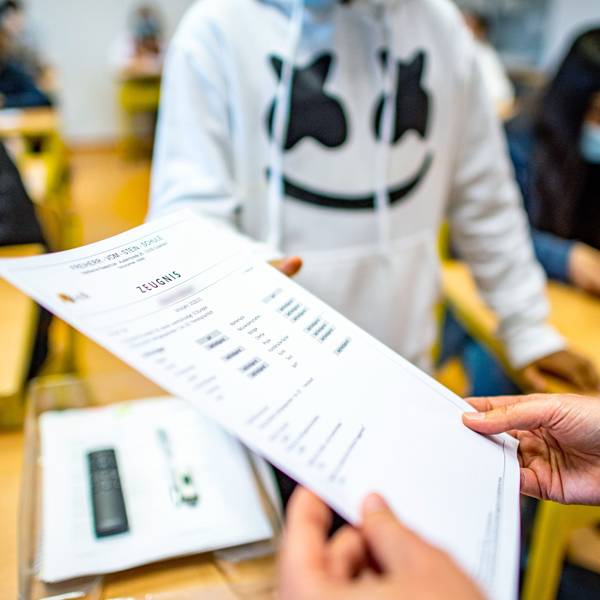 Die Klassenlehrerin übergibt das Zeugnis eines Schülers.