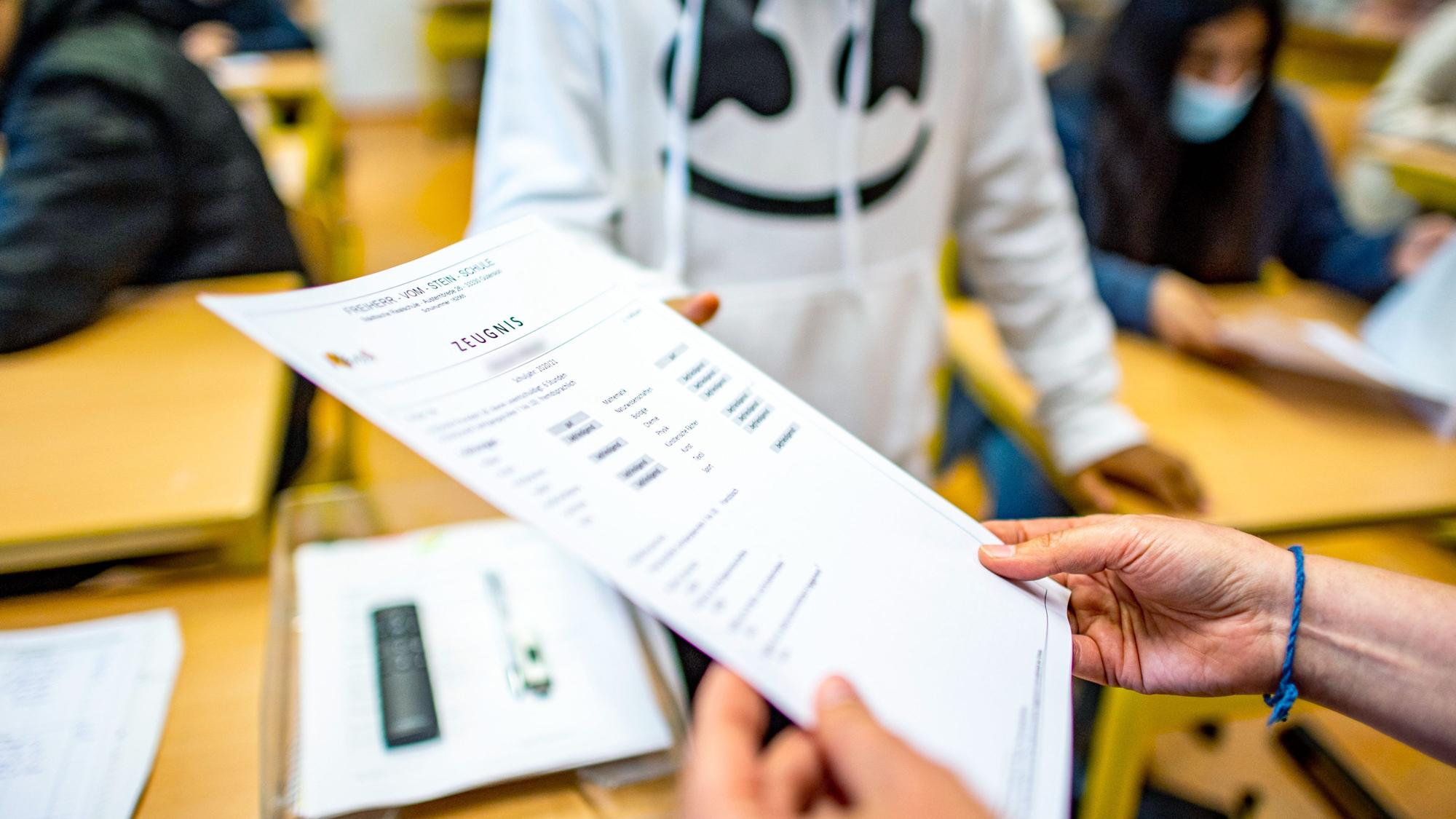 Die Klassenlehrerin übergibt das Zeugnis eines Schülers.