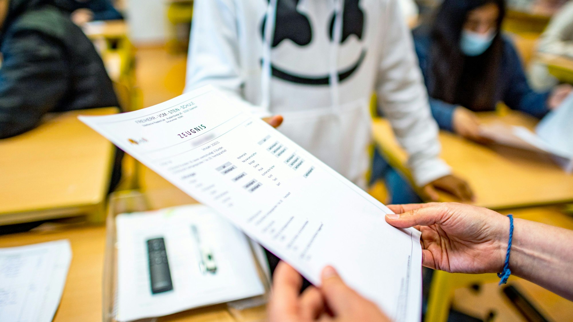 Die Klassenlehrerin übergibt das Zeugnis eines Schülers.