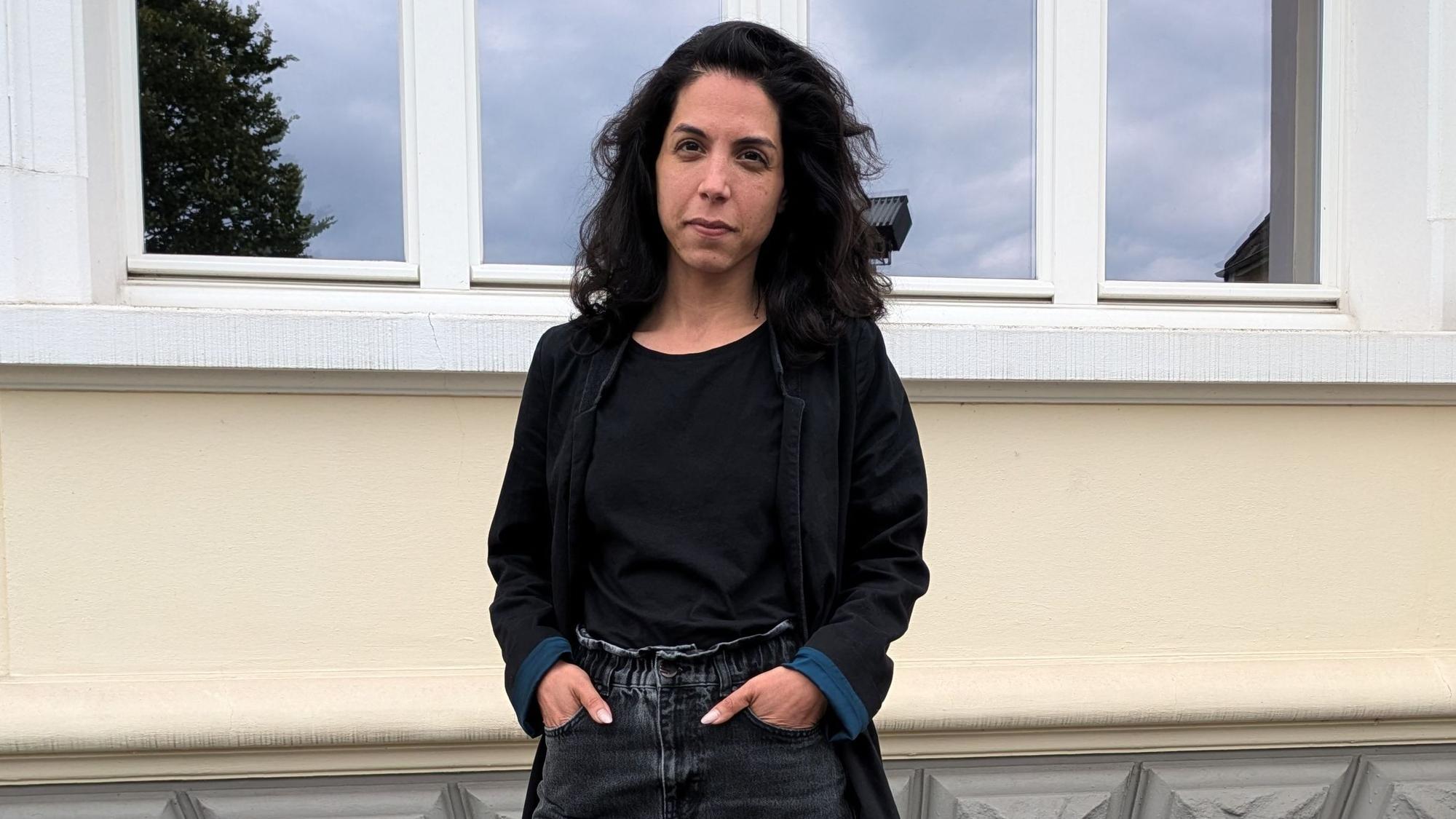 Eine Frau steht vor einer Hausfassade.