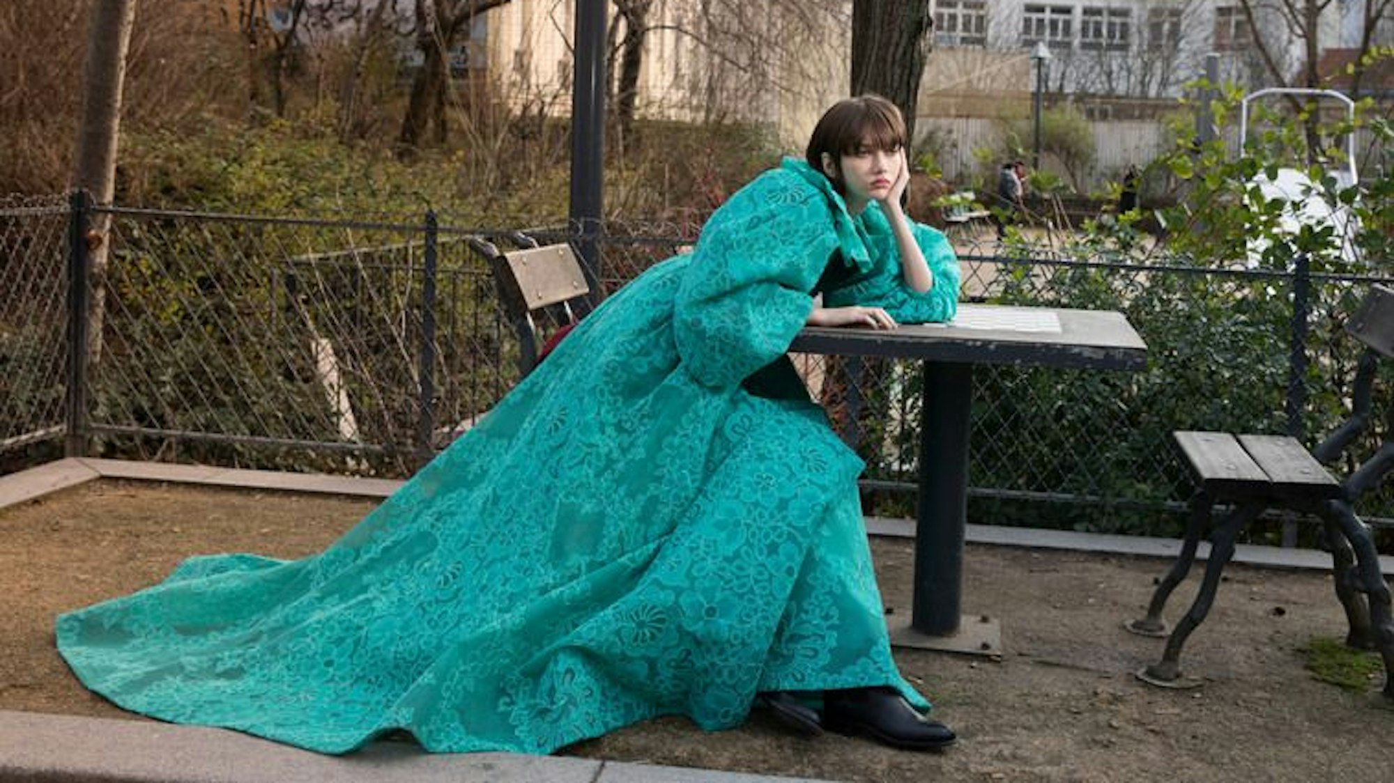 Die Aufnahme mit dem Titel „Fashion shoot for Crash Magazine“ von Jerome Sessini zeigt eine Frau in einem petrolfarbenen Kleid, die in einer gelangweilten Pose auf einer Bank sitzt und ihren Arm auf einem Tisch abstützt.