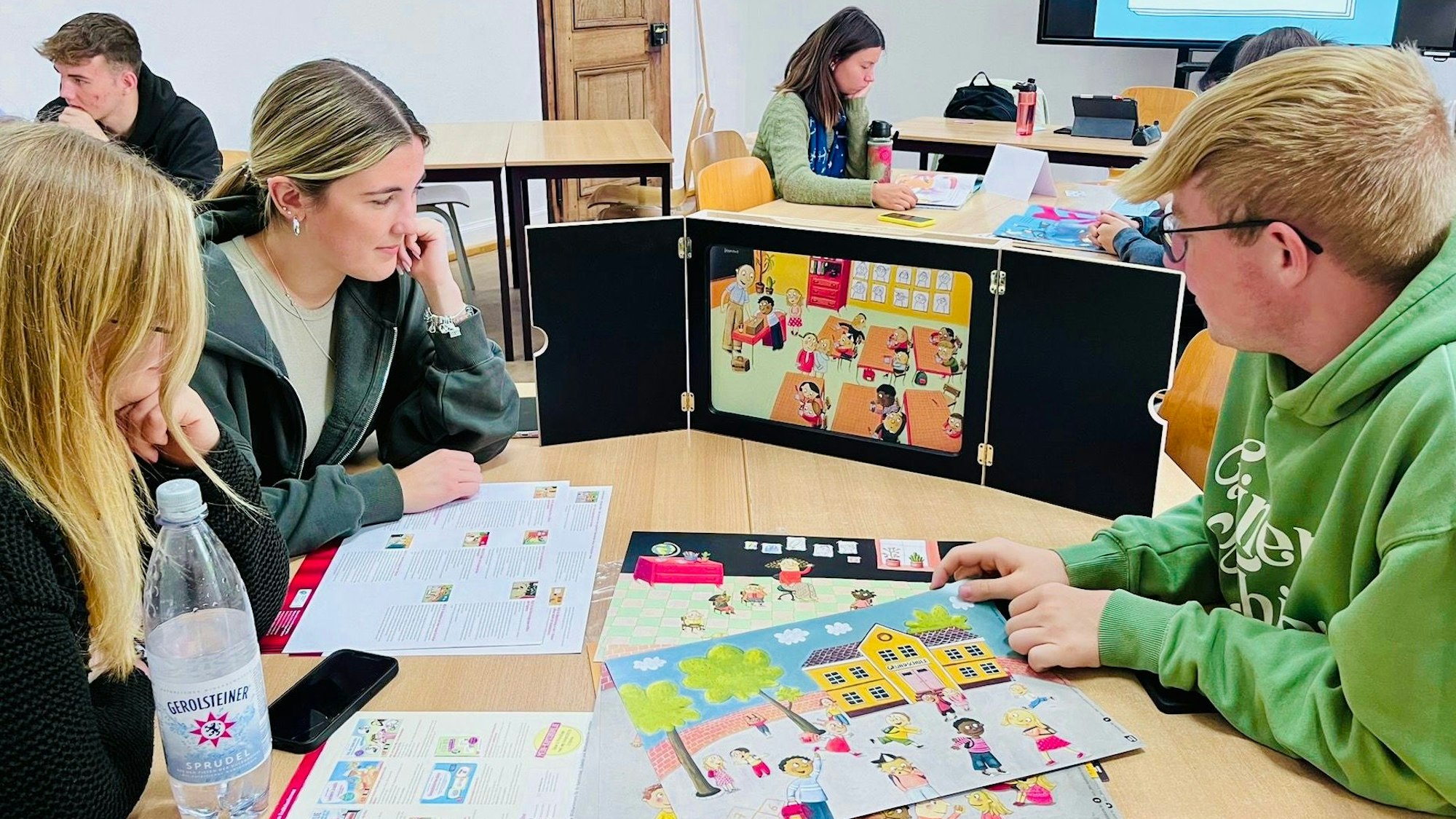 Schülerinnen und Schülern sitzen an einem Tisch, auf dem bunte Schaubilder liegen.