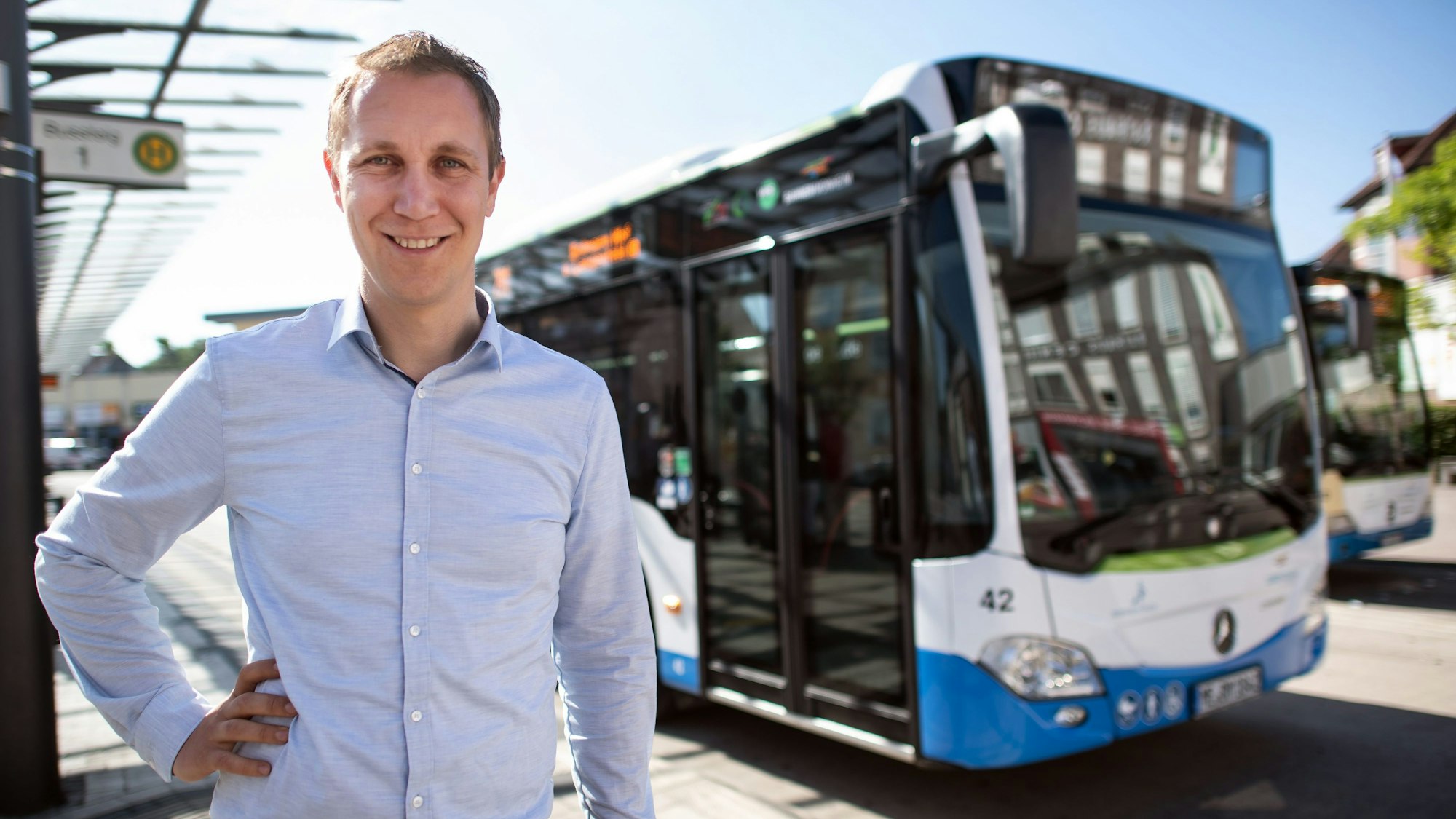Daniel Zimmermann (Peto - Die junge Alternative), Bürgermeister von Monheim, steht am Busbahnhof. Hinter ihm steht ein Bus.
