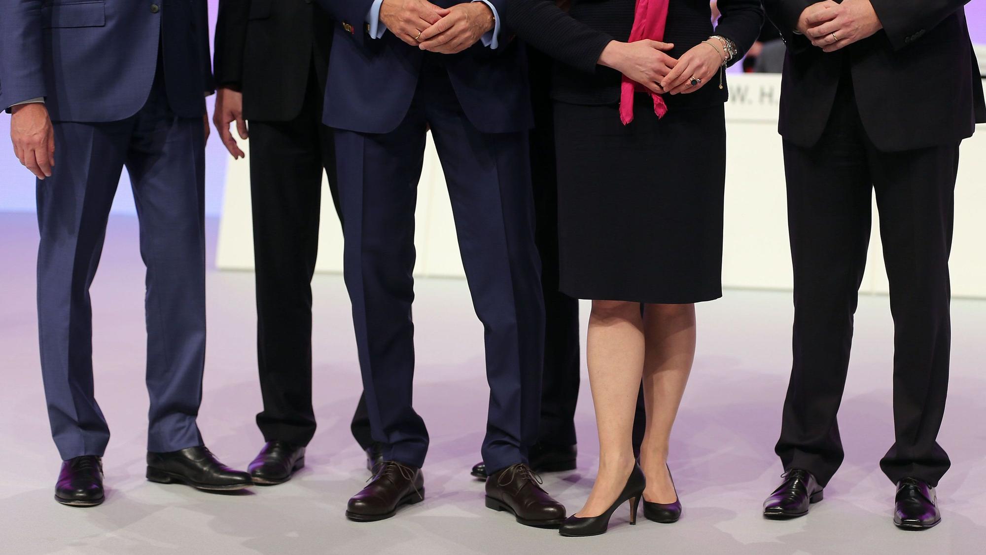 Mehrere männliche und ein weibliches Vorstandsmitglied stehen auf einer Hauptversammlung zusammen auf dem Podium.