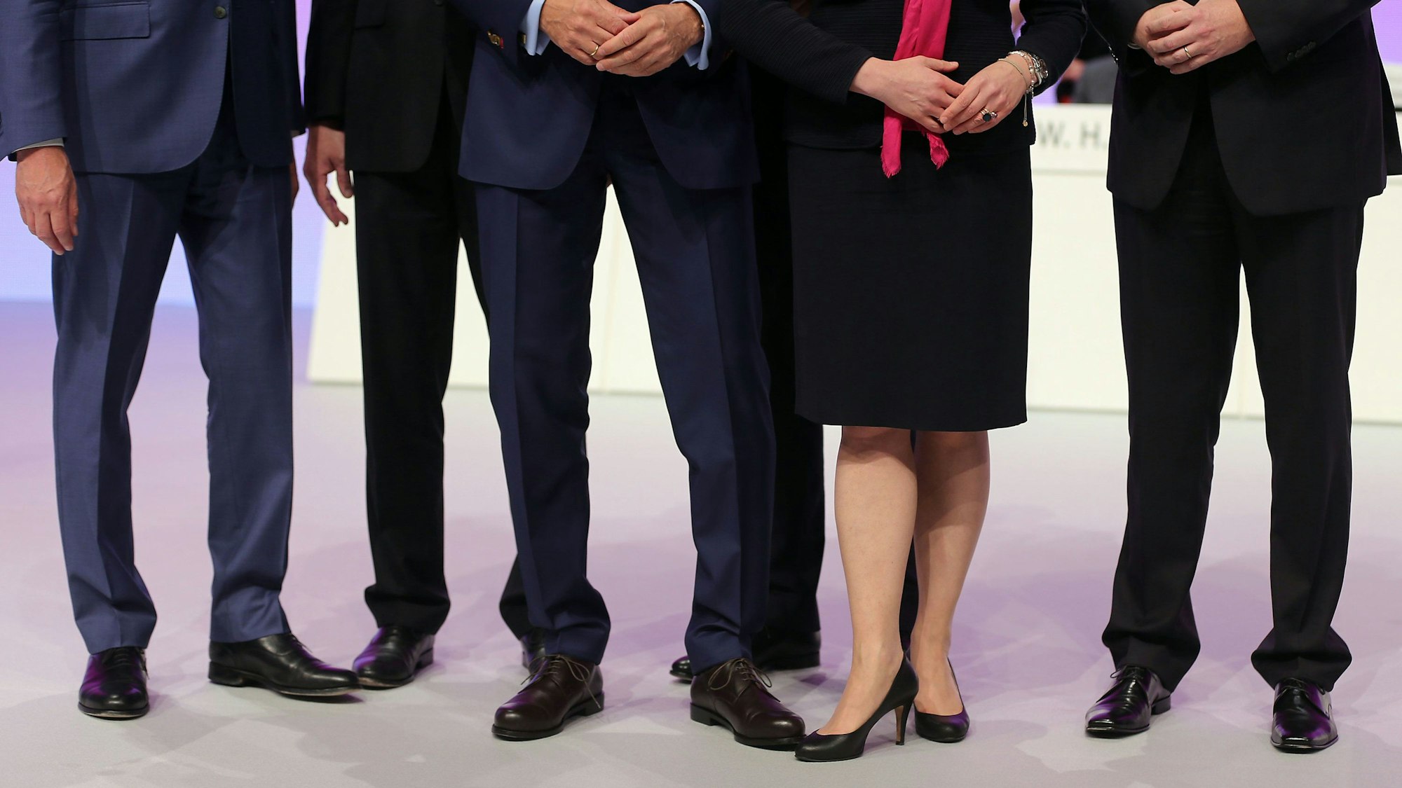 Mehrere männliche und ein weibliches Vorstandsmitglied stehen auf einer Hauptversammlung zusammen auf dem Podium.