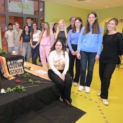 Schülerinnen und Schüler stehen neben dem Mahnmal, das sie in einem Klassenraum aufgebaut haben.