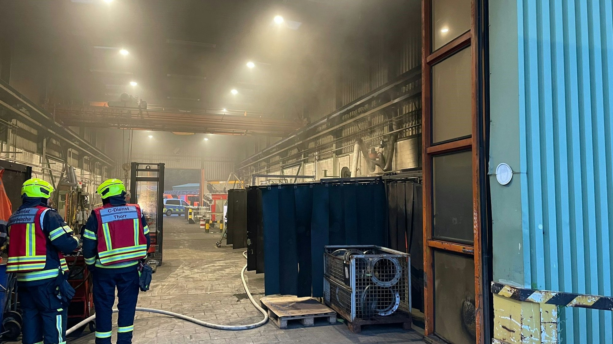 Eine verrauchte Industriehalle. Im Vordergrund Feuerwehrleute.