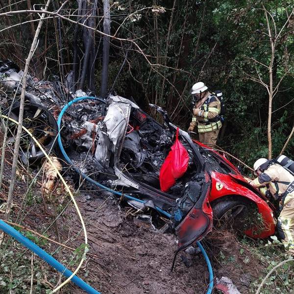 Feuerwehrleute stehen neben einem ausgebrannten Sportwagen.