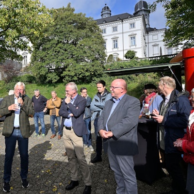 Viele Menschen stehen auf einem kleinen Platz, dahinter sieht man die Türme von Schloss Bensberg.