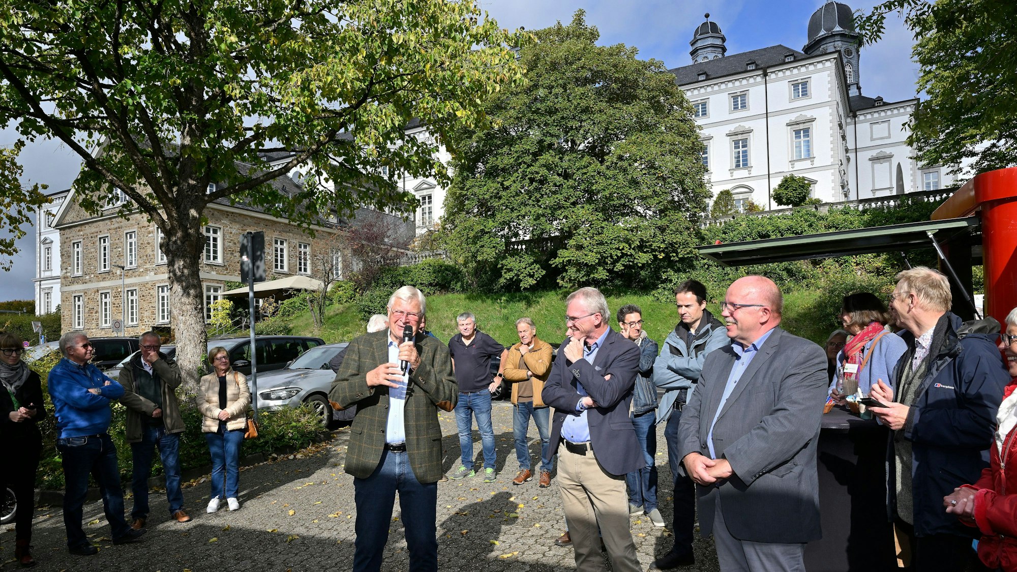 Viele Menschen stehen auf einem kleinen Platz, dahinter sieht man die Türme von Schloss Bensberg.