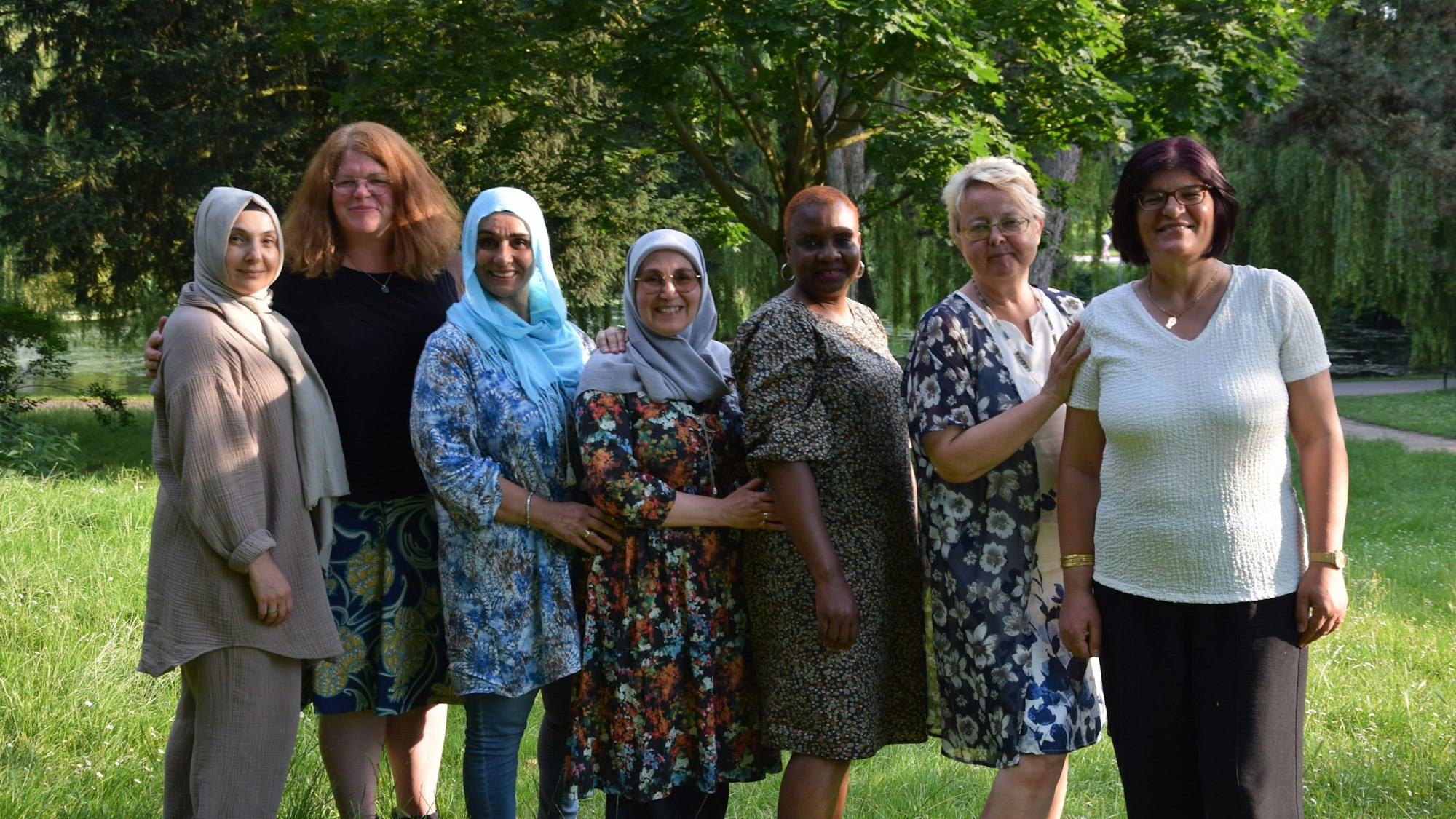 Mehrere Frauen unterschiedlicher Herkunft stehen in einem Park nebeneinander.