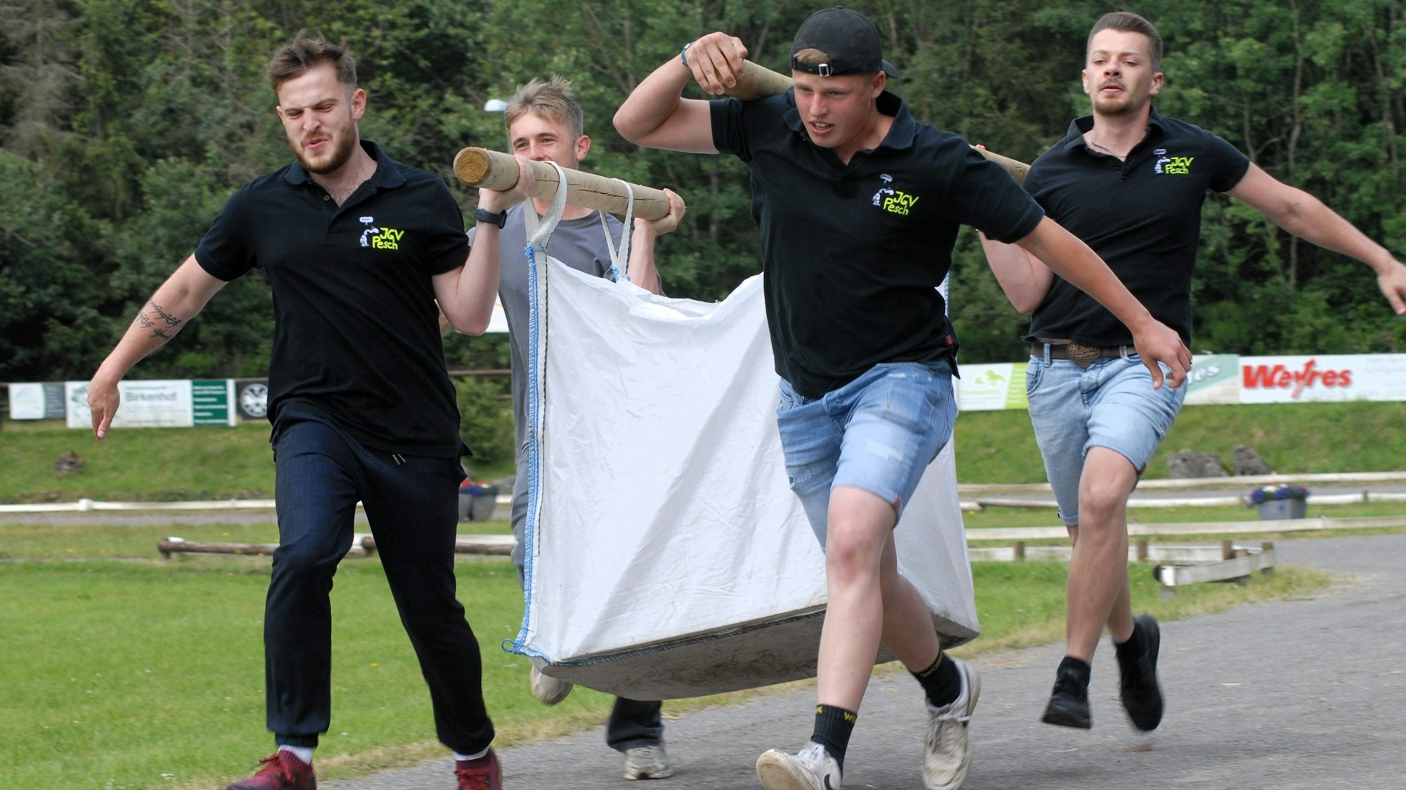 Vier junge Männer tragen ein Art Sänfte, in der ein Fünfter sitzt.