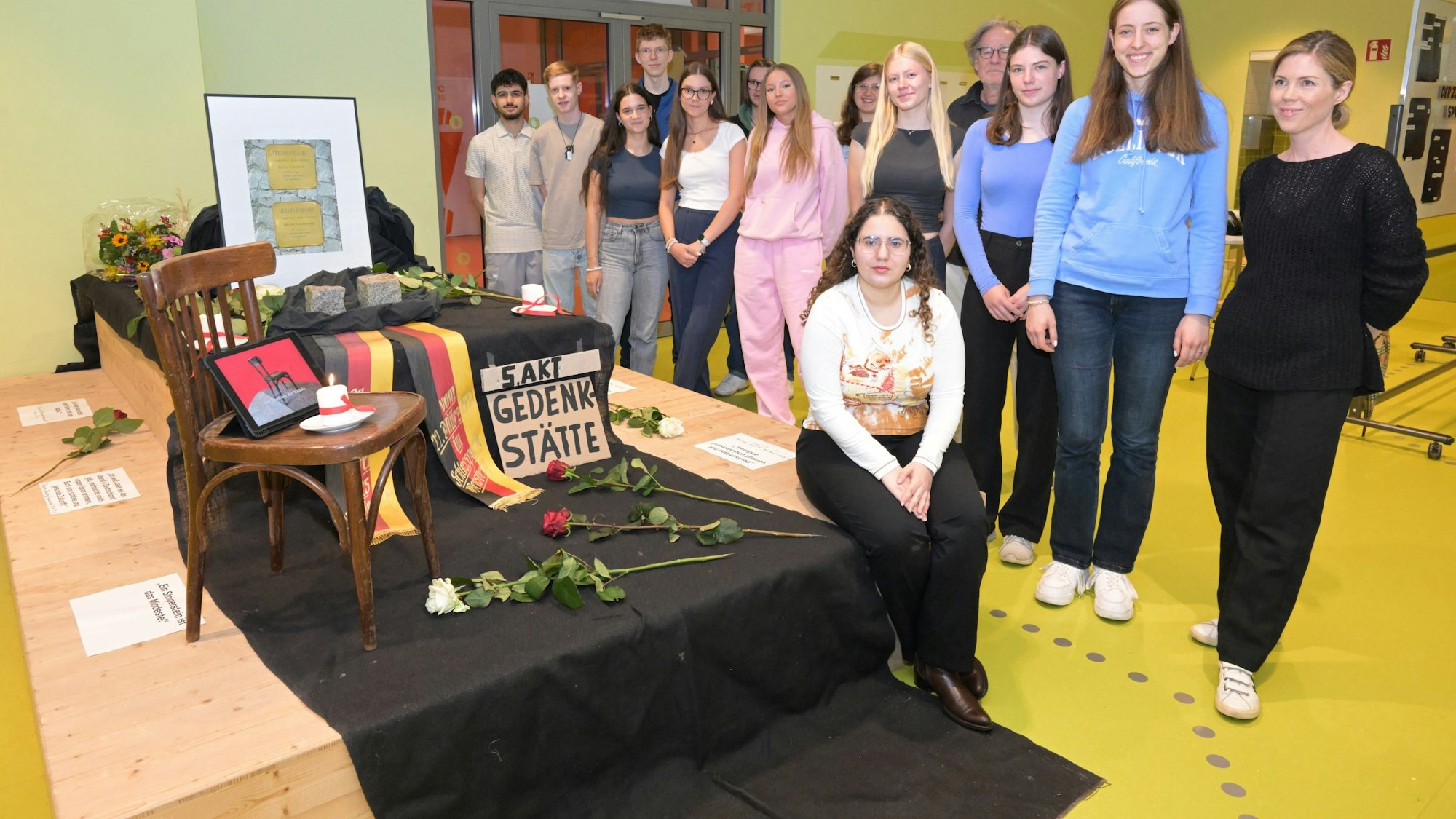Rund um das Mahnmal mit Rosen und Trauerschleifen stehen die Schüler.