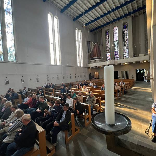 Viele Menschen sitzen in einem Kirchenschiff.