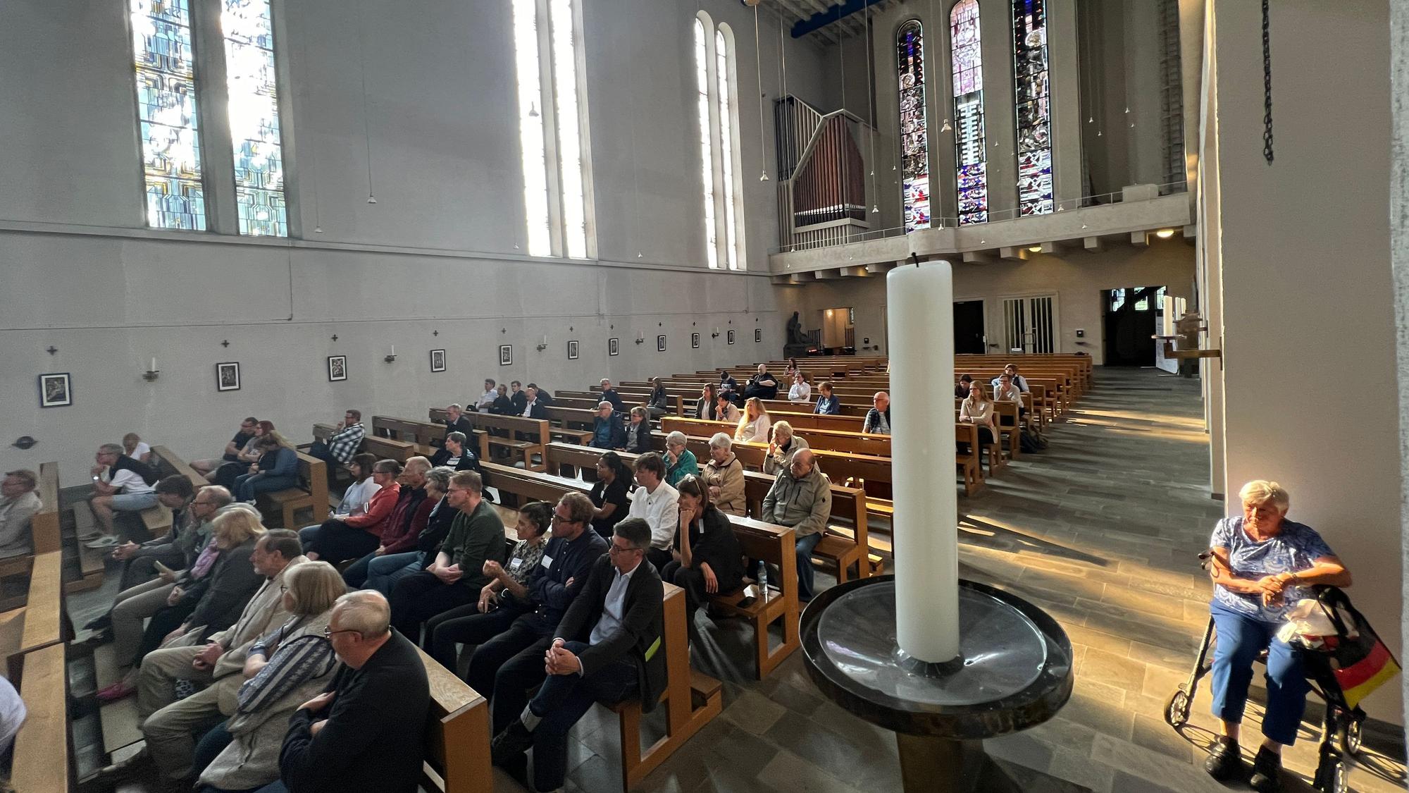 Viele Menschen sitzen in einem Kirchenschiff.