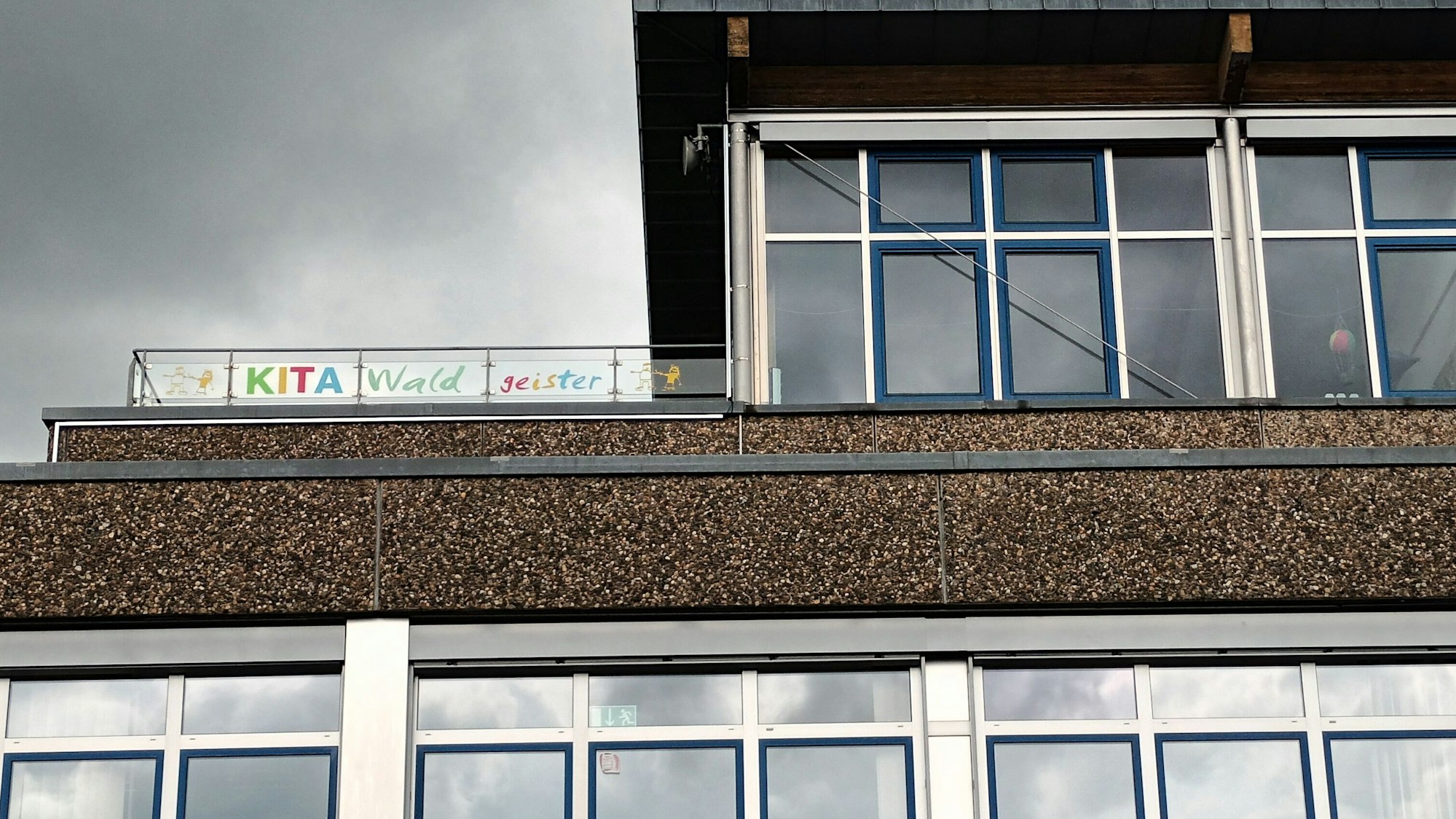 Ein Schulbau mit einem Hinweisscild auf die Kita-Nutzung im Obergeschoss.