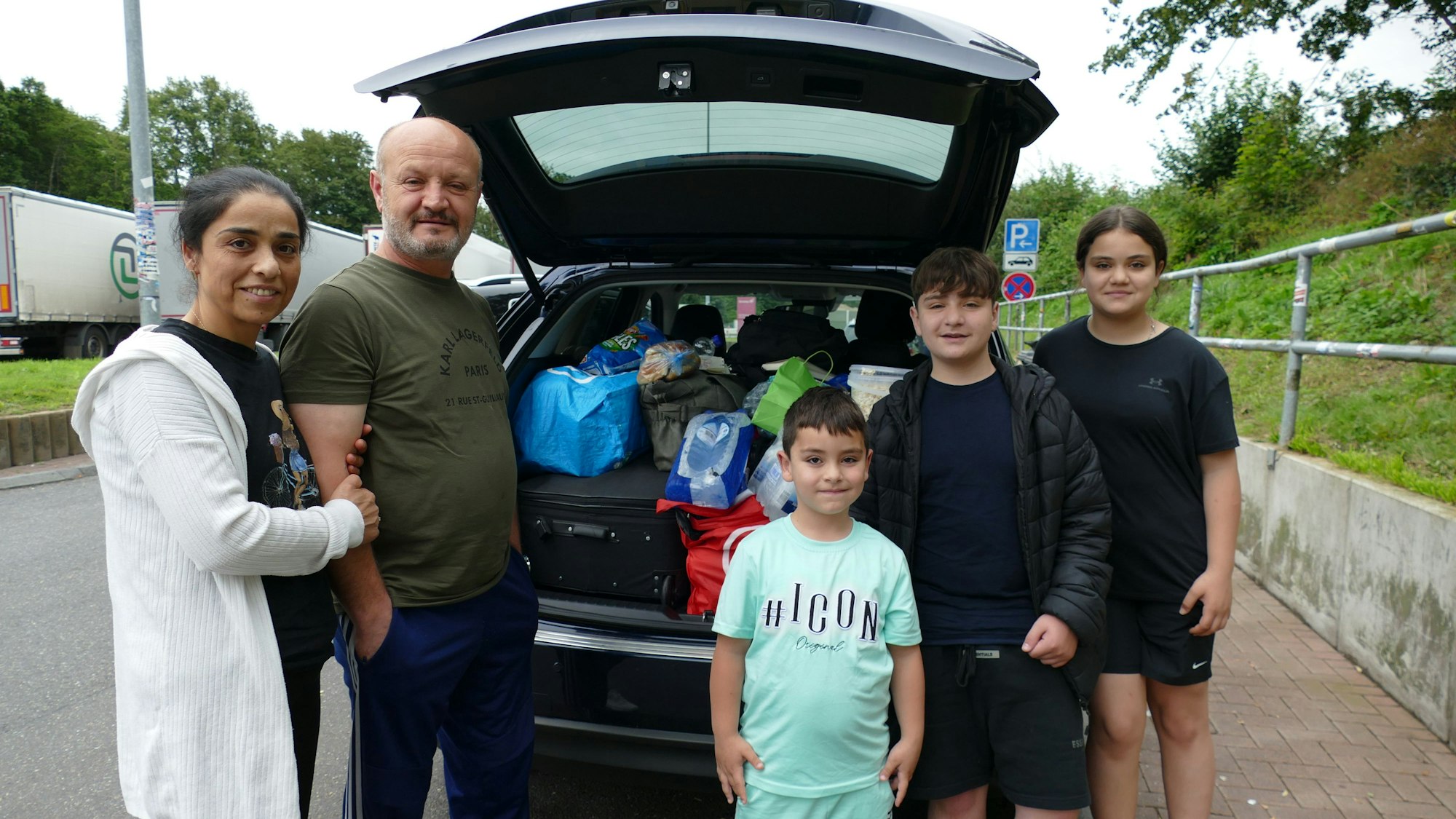 Eine Familie steht vor ihrem Auto.