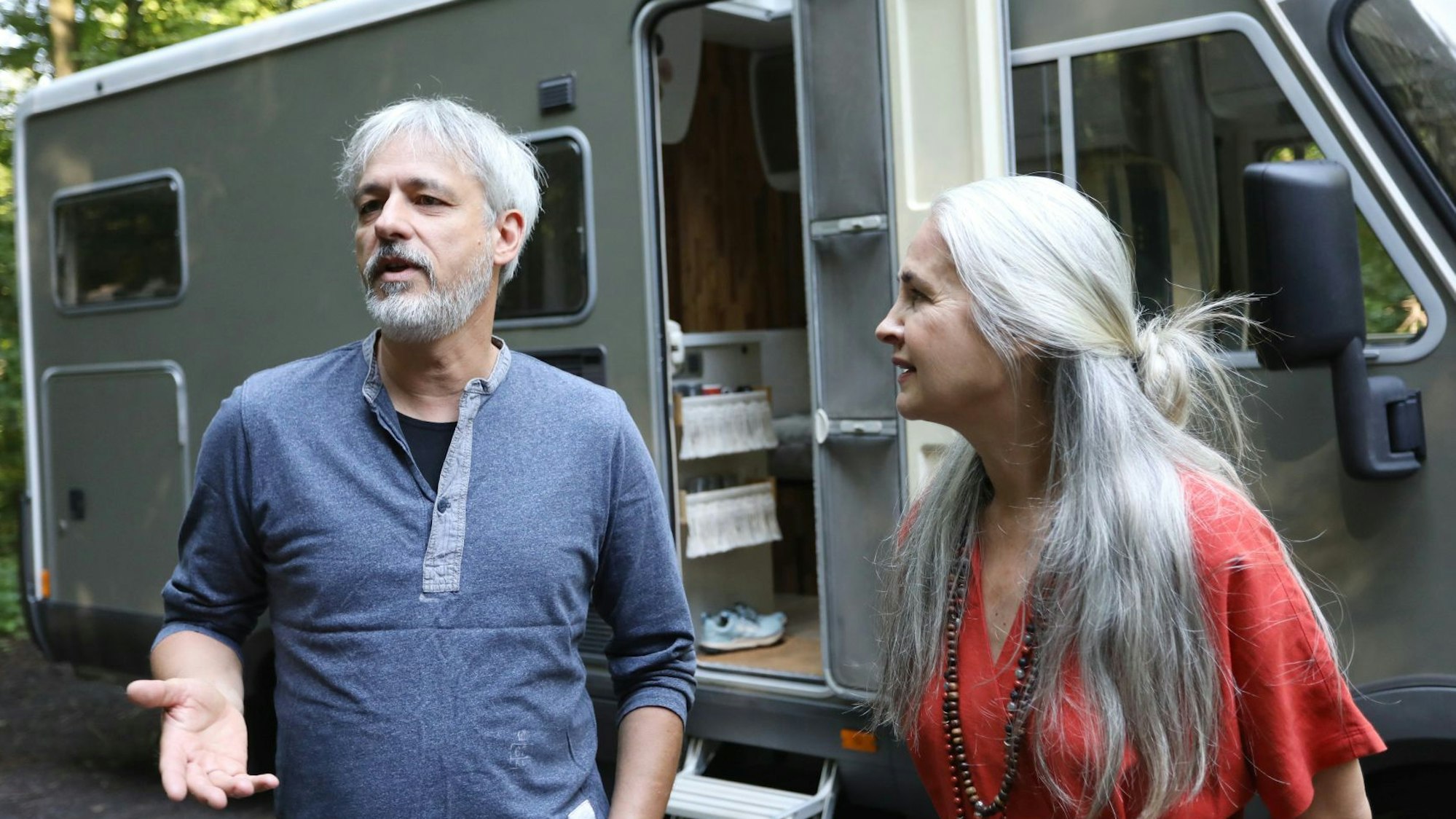 Ein Mann und eine Frau vor einem Wohnmobil, dessen Tür offensteht.