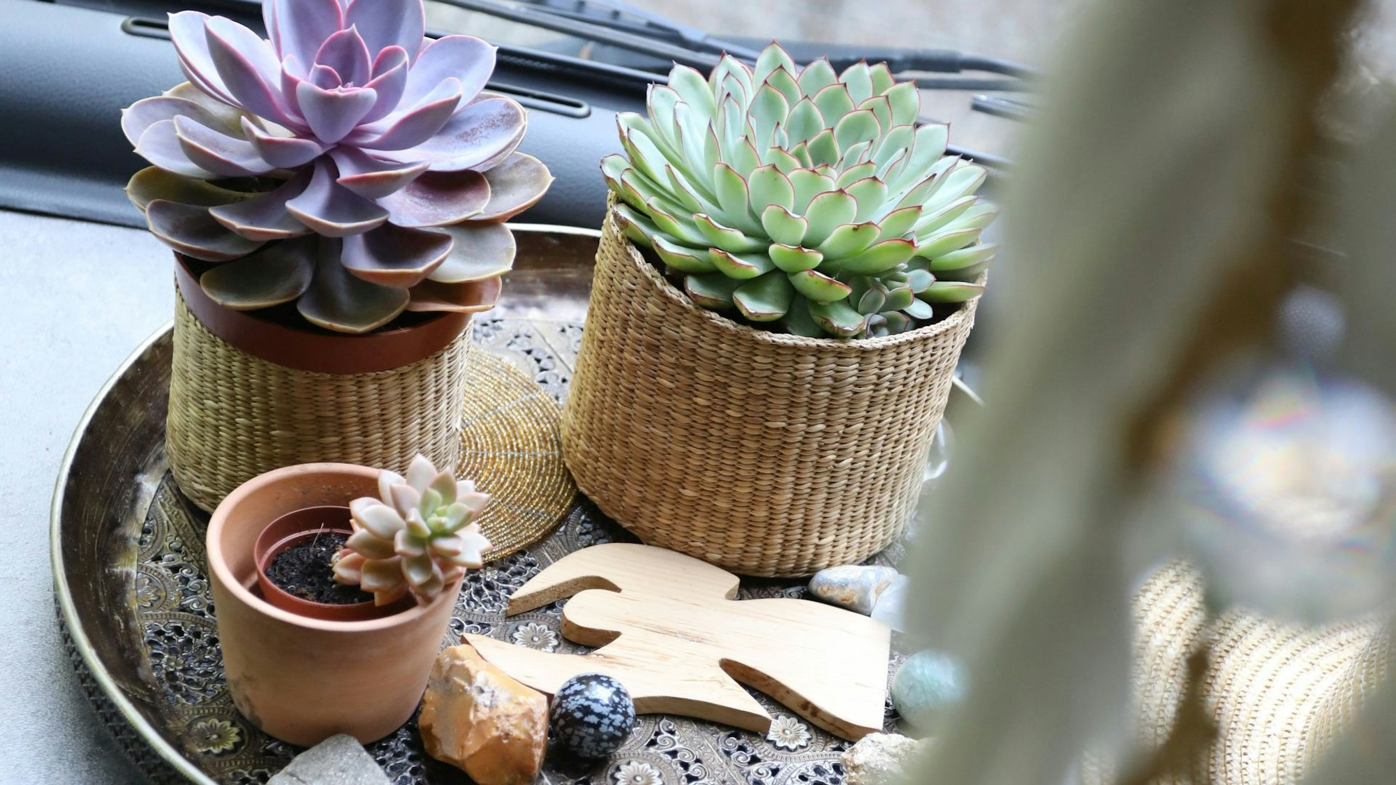 Auf einer silbernen Schale stehen Blumen, davor liegen Steine und eine Engelsfigur aus Holz.